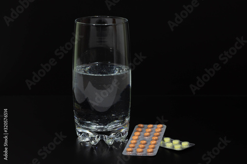 pills and glass of water on black background