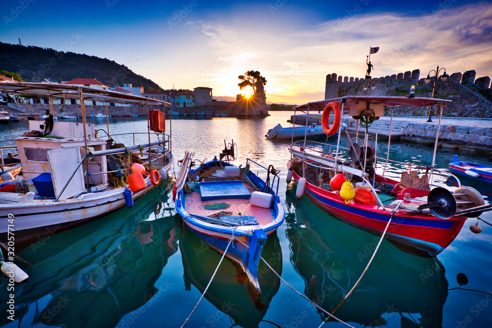 Old Greek port Nafpaktos with ancient castle walls an background and fishing boats at foreground. Epic lilac colored sunrise sky over sea scenery. Nafpaktos is famous travel destination in Greece.