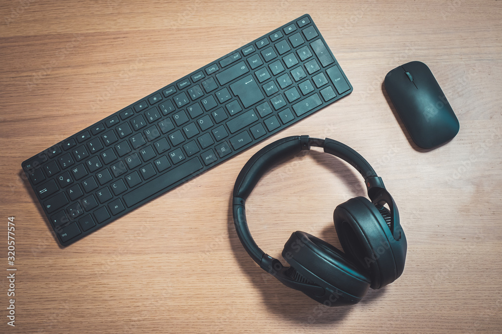 Workspace media concept: Black wireless headphones, keyboard and mouse on wooden desk Workspace media concept: Black wireless headphones, keyboard and mouse on wooden desk