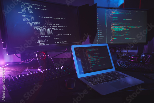 Background image of various computer equipment with programming code on screens on table in dark room, cyber security concept, copy space
