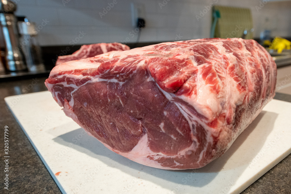 Raw prime rib beef roast laying on a white plastic cutting board on the counter of a restaurant.The meat has some marble running through it. The roast is seasoned for the barbecue. 