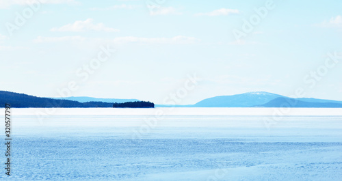 Panoramic view of the frozen lake. Snow-covered mountains and coniferous forest in the background. Clear blue sky. Kola Peninsula, Murmansk region, Polar Circle, Karelia, Russia photo
