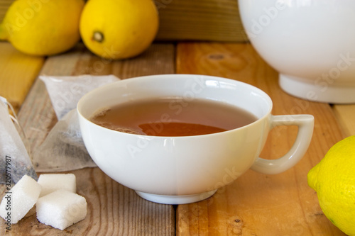 tazza di tè con teiera, zollette di zucchero, limone e bustine su fondo di legno photo