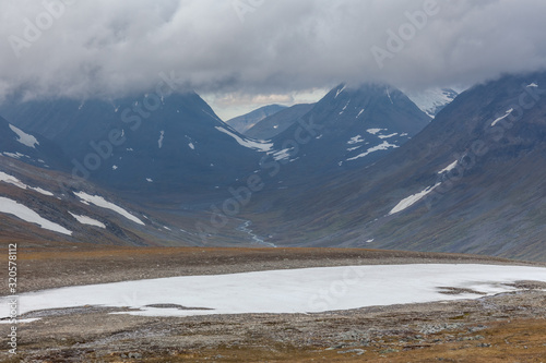 Beautiful wild nature of Sarek national park in Sweden Lapland with snow capped mountain peaks, river and lake, birch and spruce tree forest. Early autumn colors in stormy weather. selective focus