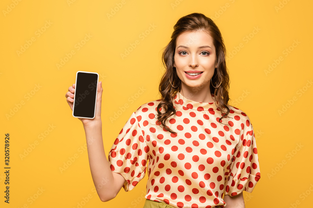 pretty young woman smiling at camera while showing smartphone with blank screen isolated on yellow pretty young woman smiling at camera while showing smartphone with blank screen isolated on yellow