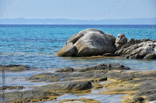 Seascape of rocky beach with azure sea water in sunny day. Amazing natural beach with white stones and turquoise water. crystal clear sea with sun reflection. Halkidiki Greece Blue Flag Beach