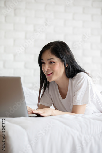 Beautiful Attractive Asian young woman lying on bed and using computer laptop for using social media and shopping online relax in cozy bedroom in holiday,Lifestyle in bedroom Concept © 220 Selfmade studio