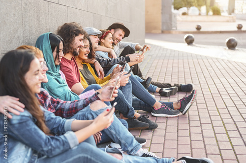 Group trendy friends using smart mobile phones outdoor - Millennial people having fun with new technology trends smartphone - Youth generation lifestyle and tech addiction social media concept photo