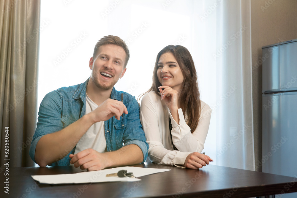 Obraz premium young happy couple man and woman sitting in their new cosy apartment after successful lease sign both smiling