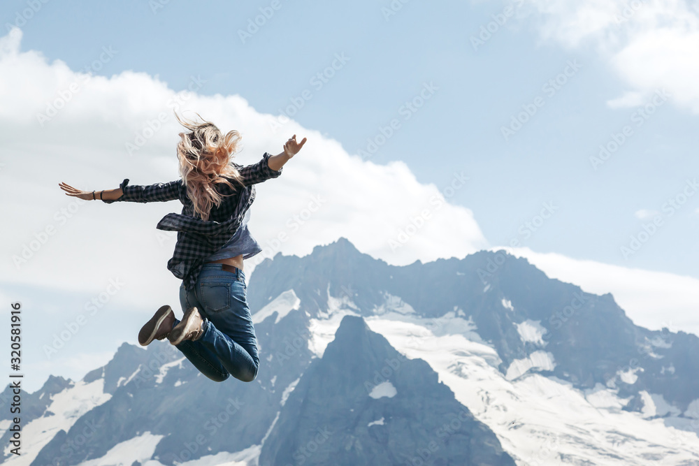 Woman hiker jumping on top of the mountain over blue skies Woman hiker jumping on top of the mountain over blue skies