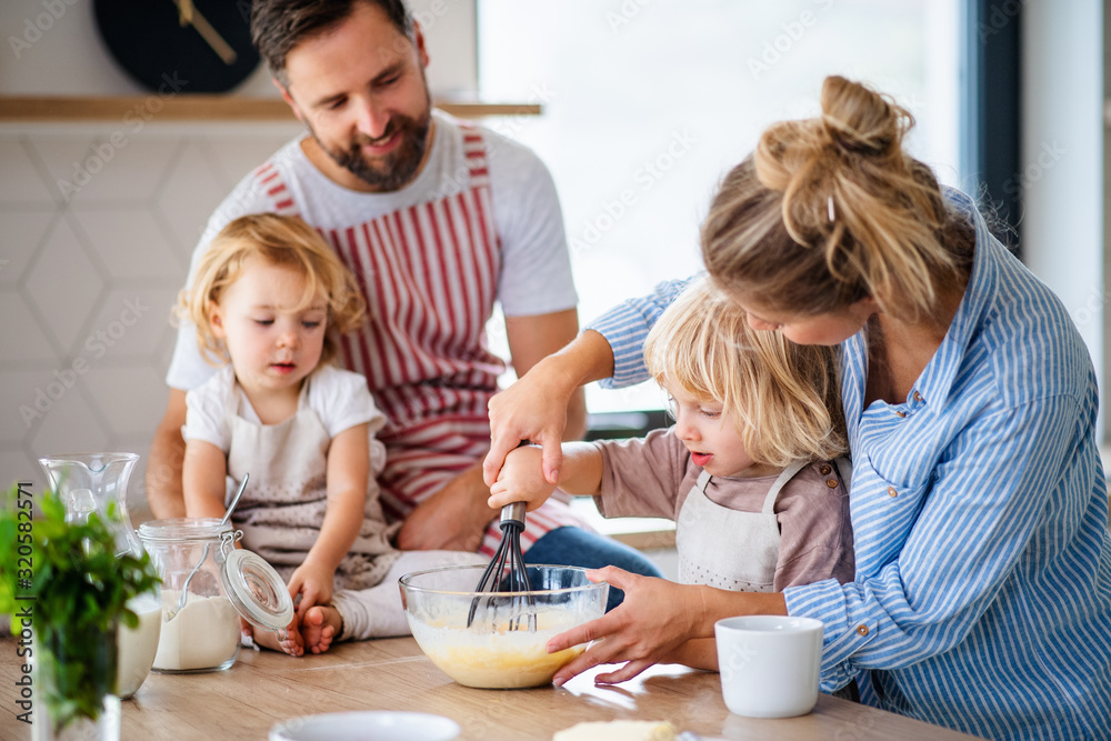 Young family with two small children indoors in kitchen, cooking. Young family with two small children indoors in kitchen, cooking.
