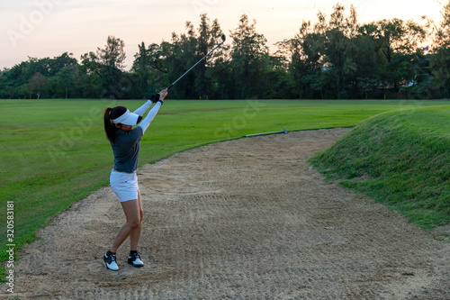 Golfer sport course golf ball fairway.  People lifestyle woman playing game golf and hitting out of sand trap go on green grass.  Asia female player game shot in summer.  Healthy and Sport outdoor