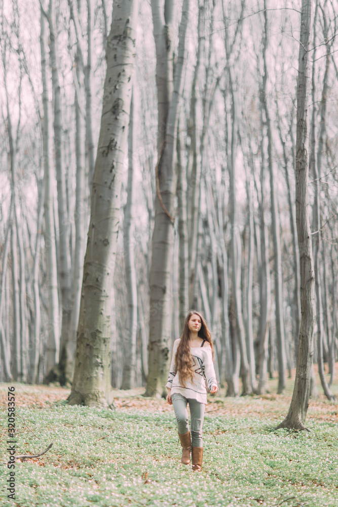Naklejka premium pretty young girl with long hair walking through the green forest in the spring