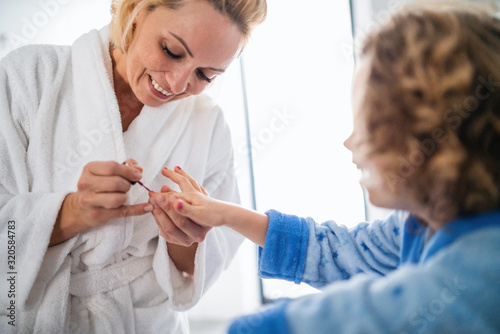 A cute small girl with mother in bathroom indoors at home  painting nails.