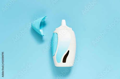Steroid nasal spray suspension w/ blank label on light blue background. Medical device used to treat allergic rhinitis, hay fever, sinusitis or nasal polyps. Health care concept. Top view.