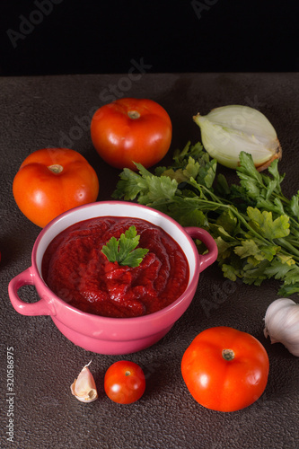 Tomato soup with parsley, onion and garlic on gray background. Comfortable food. Rustic style..