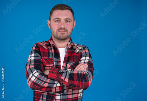Front view of man in checkered shirt with crossed arms isolated on blue background