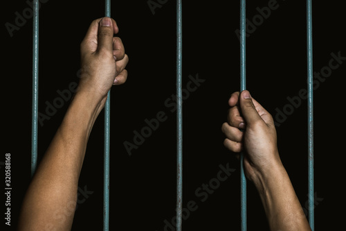 Man Hands holding iron bars in jail. Imprisoned criminal concept.