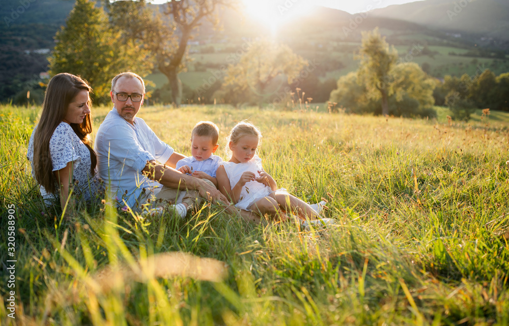 Young family with two small children sitting on meadow outdoors at sunset. Young family with two small children sitting on meadow outdoors at sunset.