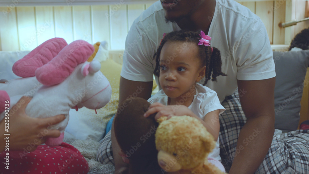 Portrait of sweet tender girl with braids sitting on fathers lap playing with favorite toys. Cheerful african family lying on comfort bed at home. family entertainment concept. Portrait of sweet tender girl with braids sitting on fathers lap playing with favorite toys. Cheerful african family lying on comfort bed at home. family entertainment concept.