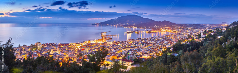 Panoramic city and port view on the island of Zakynthos, Greece. Incredibly romantic sunrise on Zakinthos. Amazing sunset view on Zante town with multicolored clouds. Street lights. Port with ferries