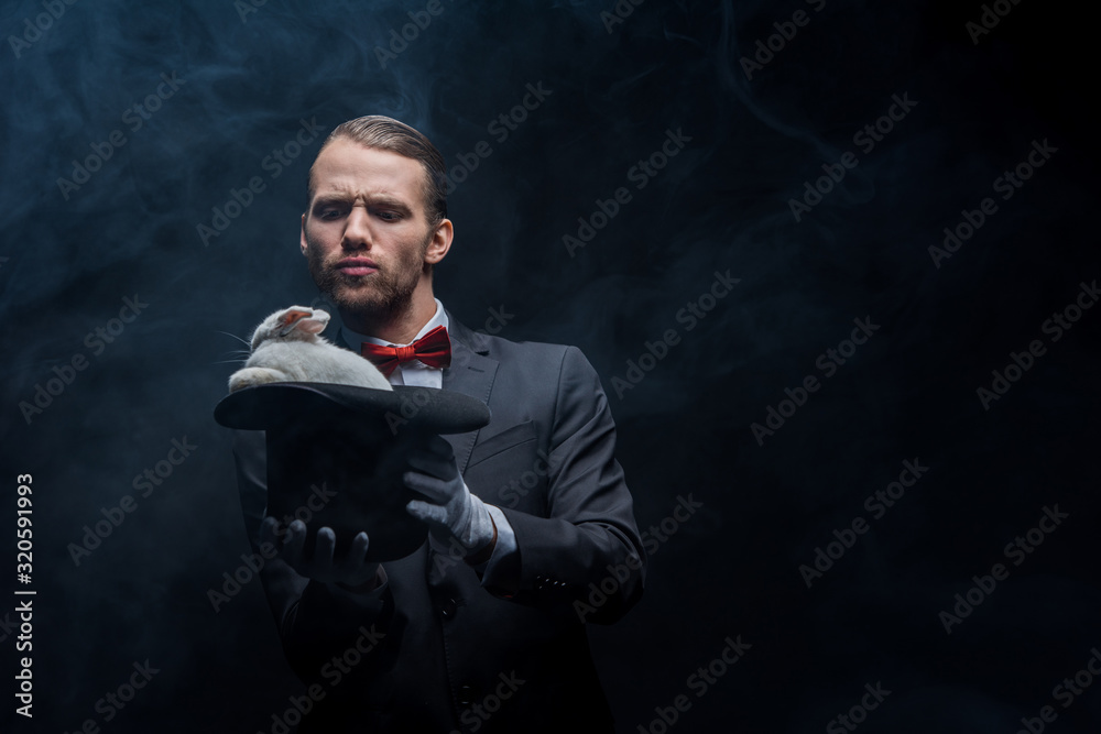 emotional magician in suit showing trick with white rabbit in hat, dark room with smoke emotional magician in suit showing trick with white rabbit in hat, dark room with smoke