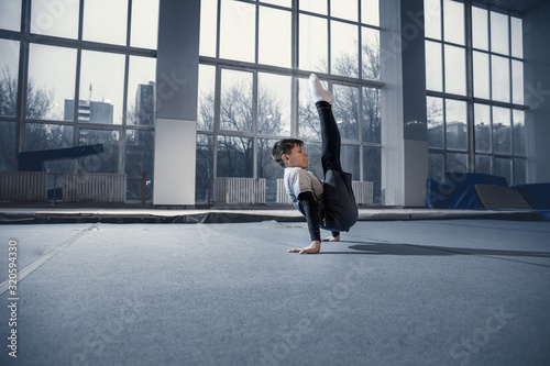 Little male gymnast training in gym  flexible and active. Caucasian fit little boy  athlete in sportswear practicing in exercises for strength  balance. Movement  action  motion  dynamic concept.