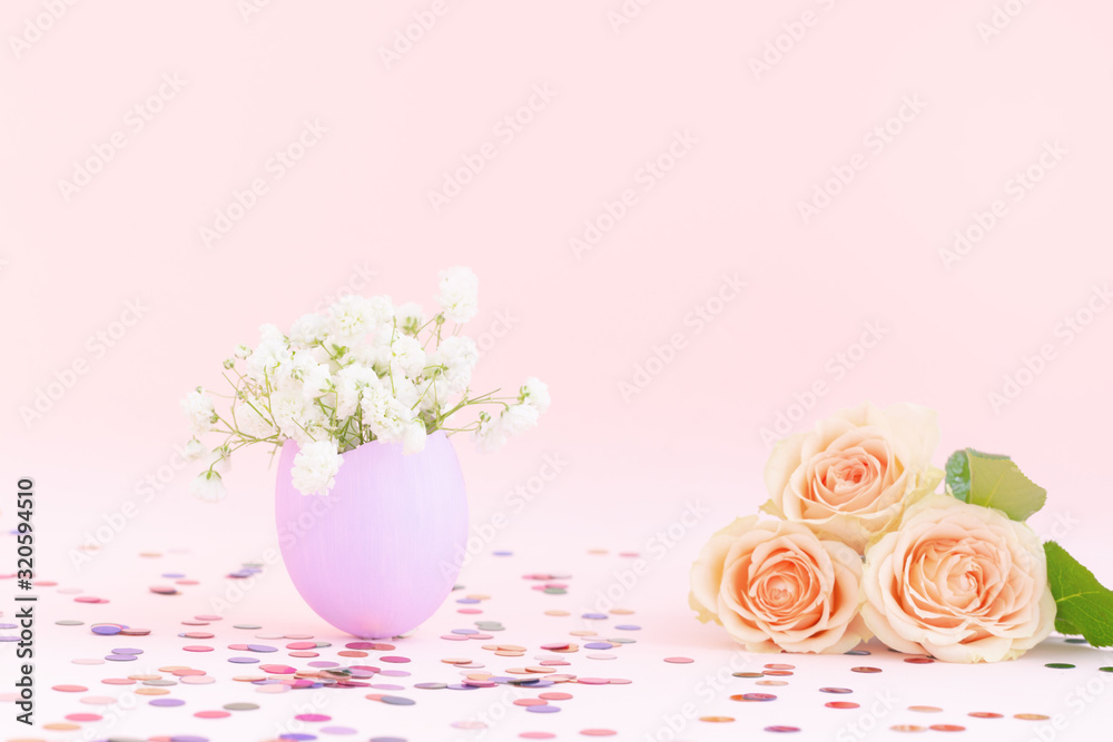 Purple easter eggshell with white gypsophila,yellow,orange pastel roses, pink background,multicolor confetti. Egg is symbol of celebration of religious holiday among Catholics, Christians,Protestants