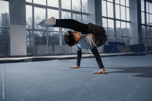 Little male gymnast training in gym  flexible and active. Caucasian fit little boy  athlete in sportswear practicing in exercises for strength  balance. Movement  action  motion  dynamic concept.