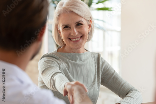 Фотография Smiling middle-aged female employee handshake greeting at meeting