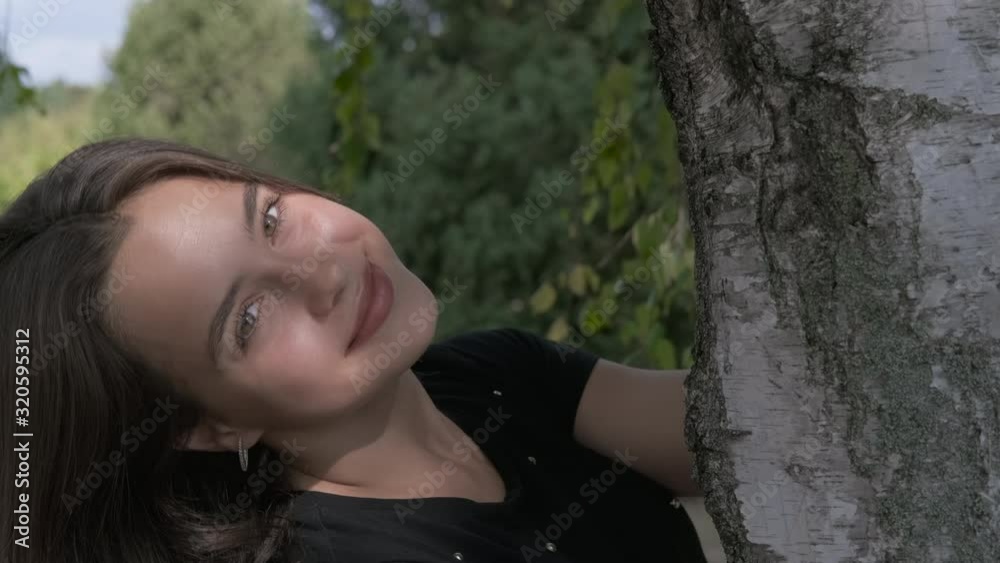 With camera by the tree trunk. Charming young girl at the trunk of a tree. With camera by the tree trunk. Charming young girl at the trunk of a tree.