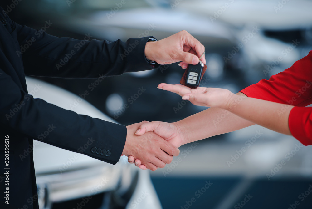 Businessman giving car key while shaking a customer hand at new car showroom