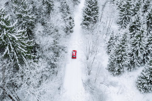 Aerial top view of snow covered forest with winter road and red car.