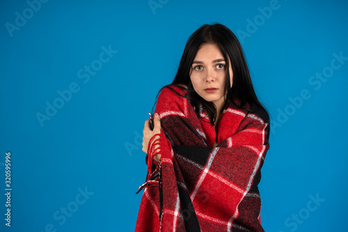 Front view of girl wrapping in warm checkered blanket isolated on blue background