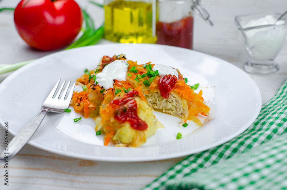 Homemade cabbage rolls with carrots, red tomato sauce and cream on a white plate