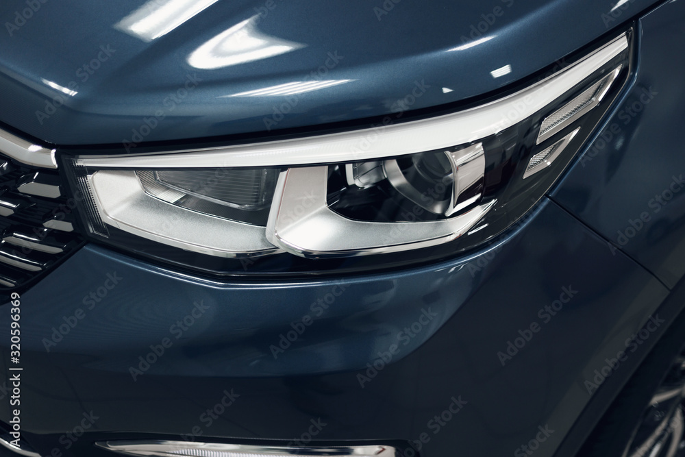 Close-up headlights of a modern blue color car. Detail on the front light of a car. Modern and expensive car concept. The car is in the showroom. Automotive concept. Classic blue color