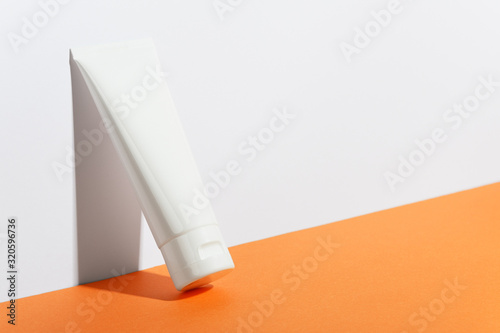Obraz na płótnie Cream tube on bright sunny orange background. Cosmetic skincare product blank plastic package. White unbranded lotion, balsam, hand creme, toothpaste mockup. Sunscreen cream bottle w salonie