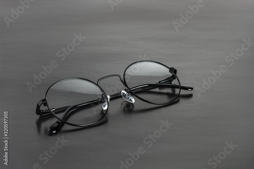 The round black metal medical eye glasses with folded temples on a black background