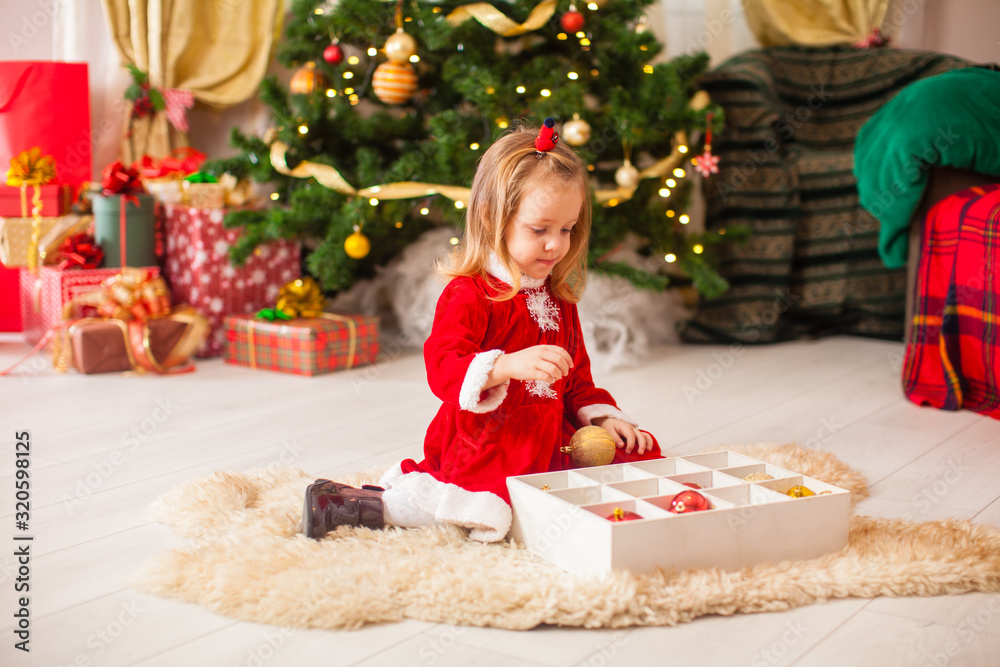 Cute little girl decorating a Christmas tree with colorful baubles at home