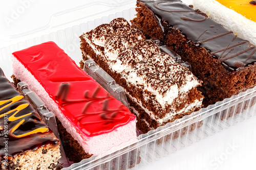 Assorted Tiramisu cakes in transparent plastic box on white background close-up