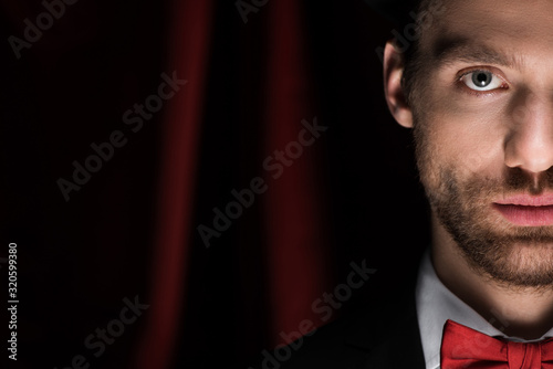 handsome magician in black suit in circus with red curtains