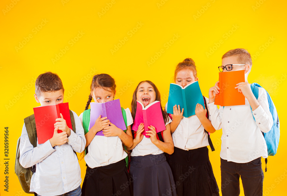 Happy schoolkids standing with colorful books isolated on yellow background. Kids hiding face behind books Happy schoolkids standing with colorful books isolated on yellow background. Kids hiding face behind books