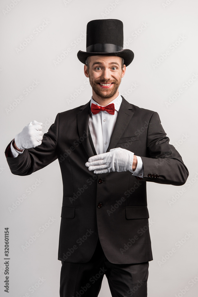 cheerful magician showing trick with finger, isolated on grey cheerful magician showing trick with finger, isolated on grey