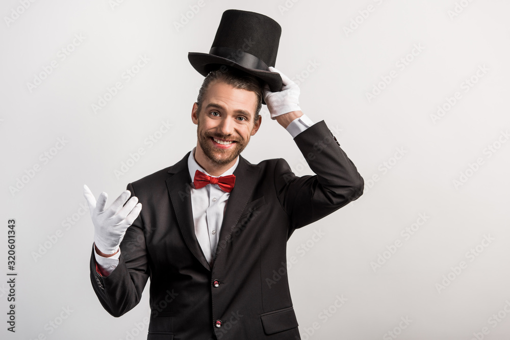 smiling magician in gloves wearing hat, isolated on grey smiling magician in gloves wearing hat, isolated on grey
