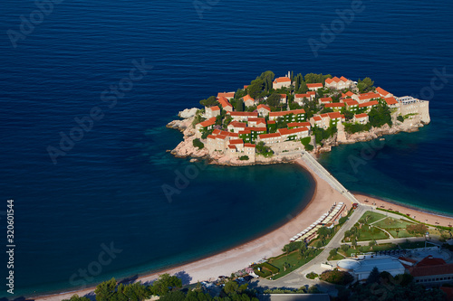 Amaizing aerial view on Sveti Stefan Island City. Small islet and resort in Montenegro. Balkans, Adriatic sea, Europe. Sunny day on the beach near the Saint Stefan island. Bridge on the old town.