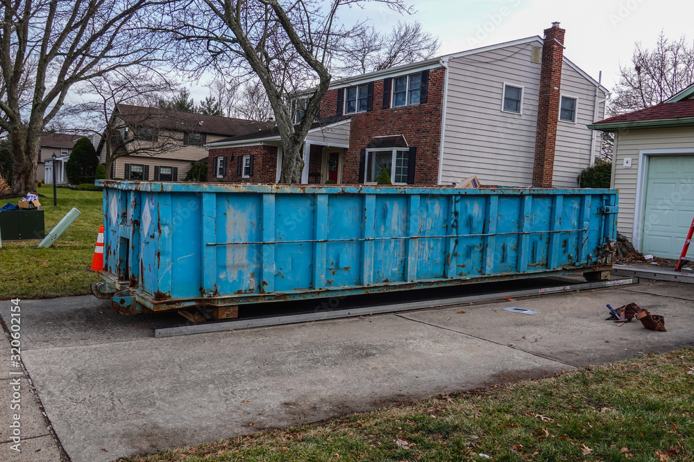 Blue dumpster in the driveway of a residential home that is undergoing renovation Blue dumpster in the driveway of a residential home that is undergoing renovation