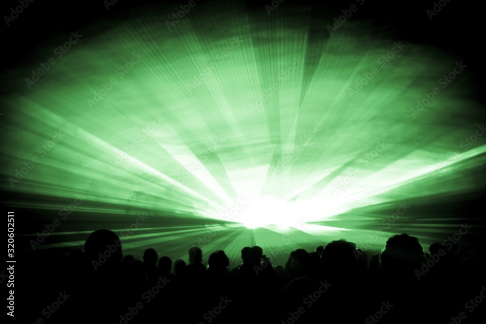 Green laser show nightlife club stage with party people crowd. Luxury entertainment with audience silhouettes in nightclub event, festival or New Years Eve. Beams and rays shining colorful lights
