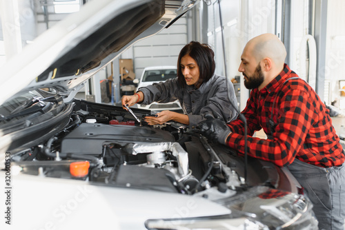 Auto car repair service center. Mechanic examining car engine. Female Mechanic working in her workshop. Auto Service Business Concept. Pro Car female Mechanic Taking Care of Vehicle. © Serhii