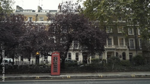 Traditional red telephone boxes in London standing on the street near the road against the trees. National symbols of England photo
