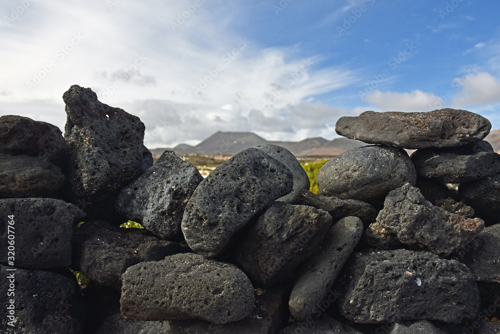 Volcanic stone wall with blurred volcano in background, Lanzarote, Spain Volcanic stone wall with blurred volcano in background, Lanzarote, Spain